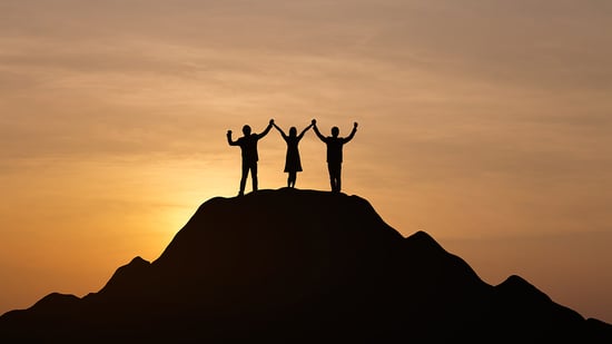 Three people standing in celebration on top of mountain
